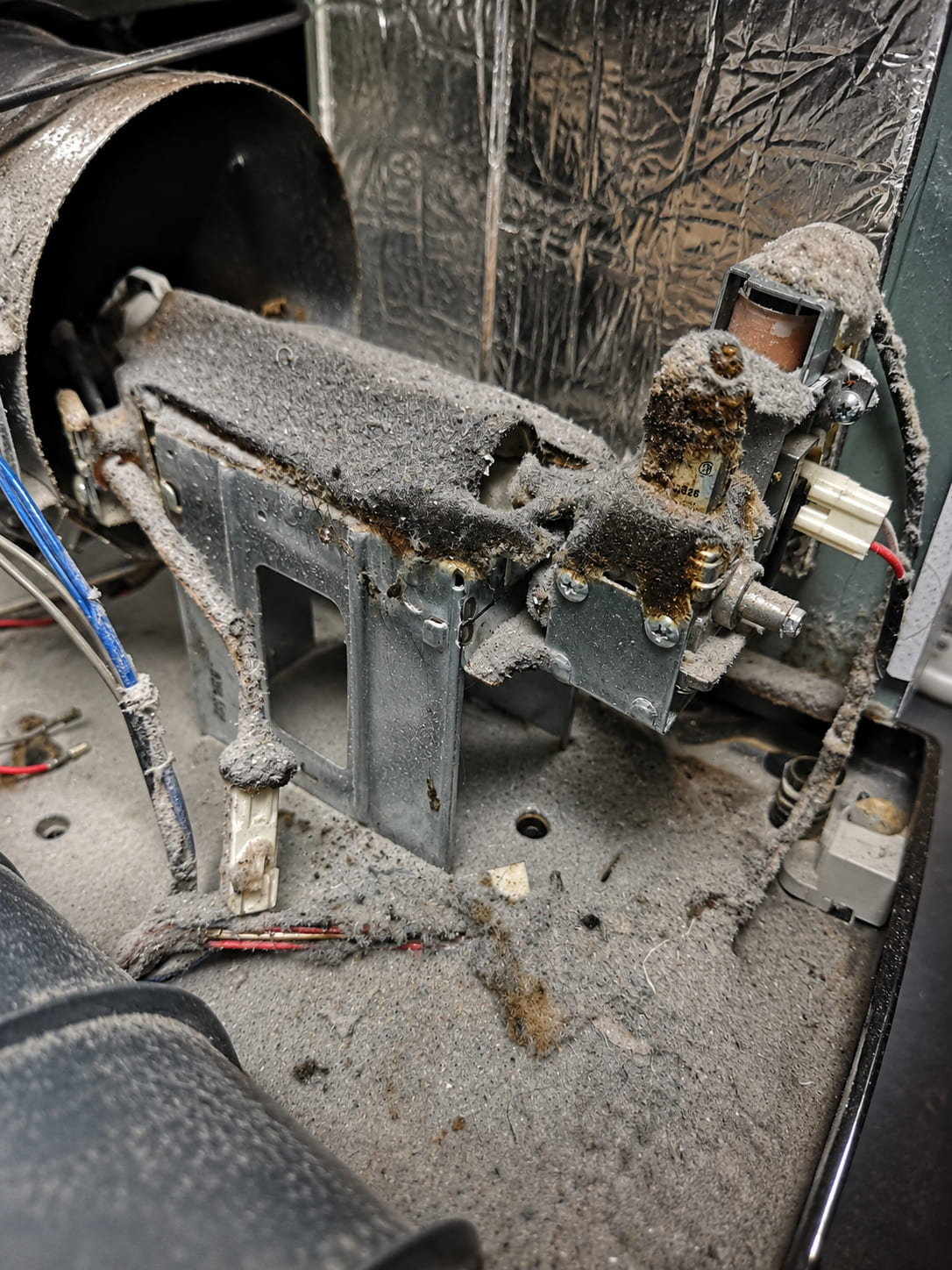 The burner area inside a dryer, felted over with thick grey lint and stained dark brown where it has been scorched by heat