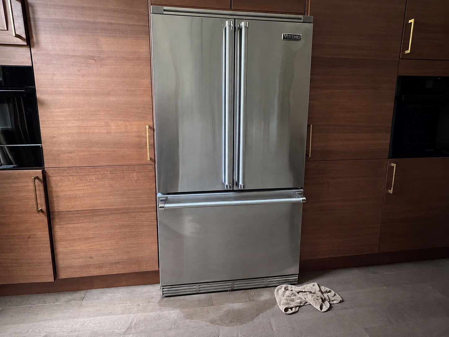 Water pooled on the floor in front of a Viking refrigerator, with a towel soaking it up