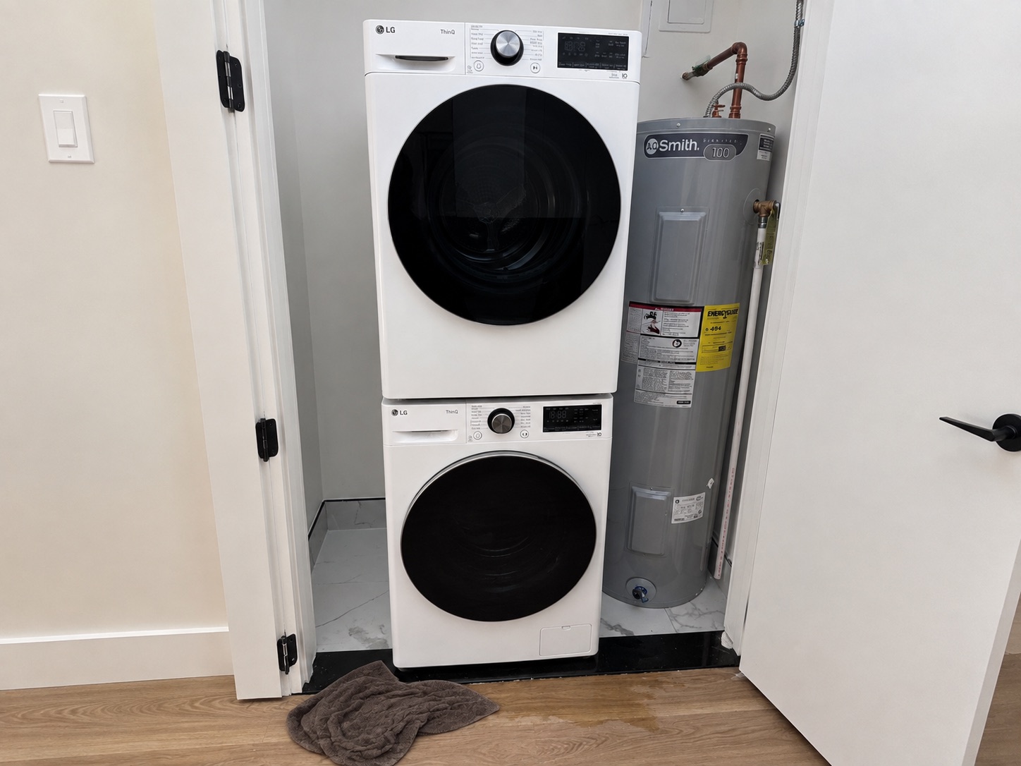 A stacked washer and dryer in a closet with a towel on the floor where the machine leaked