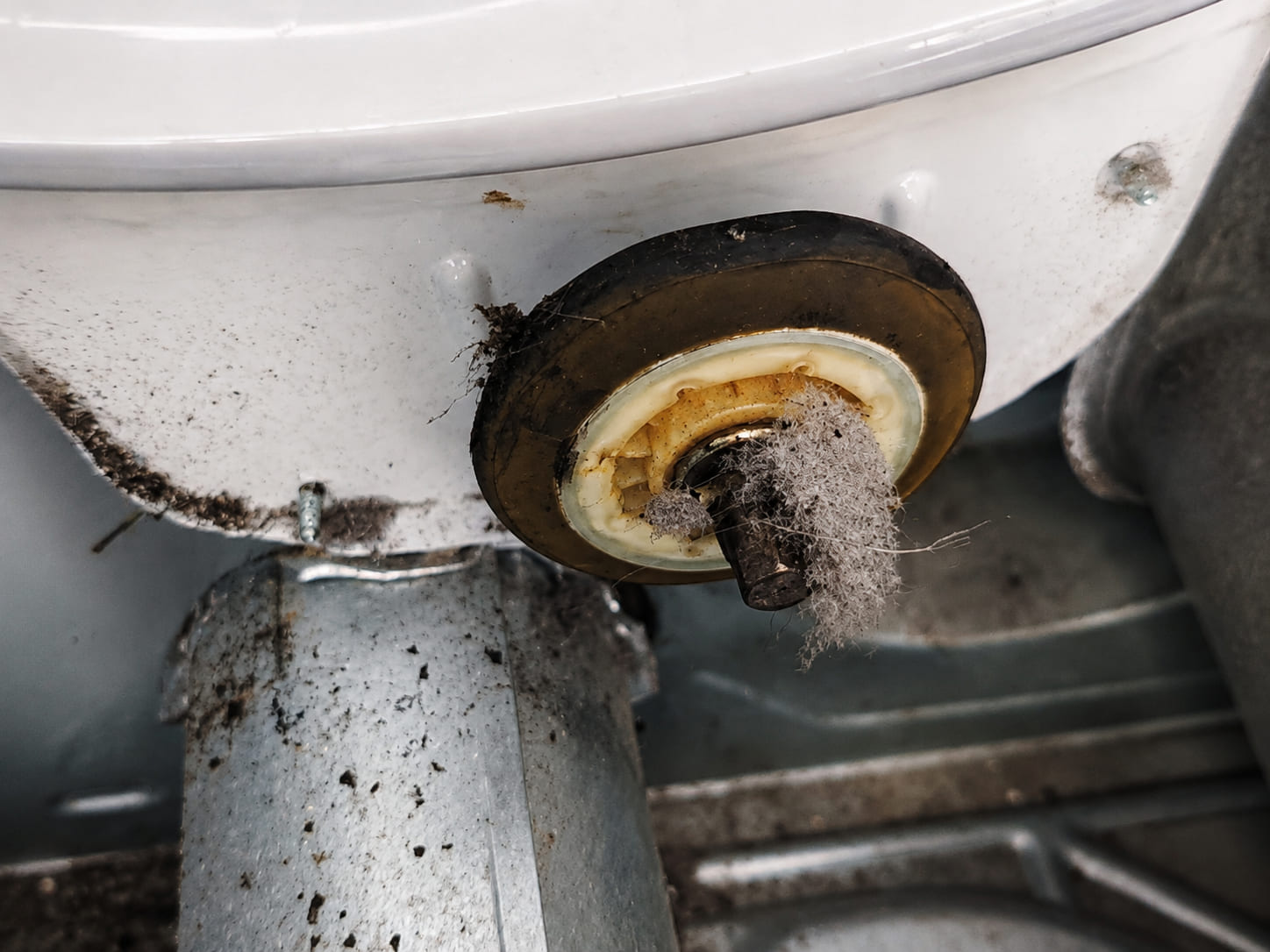 A worn drum support roller inside a dryer, discoloured from heat, with a wad of lint wound around its shaft