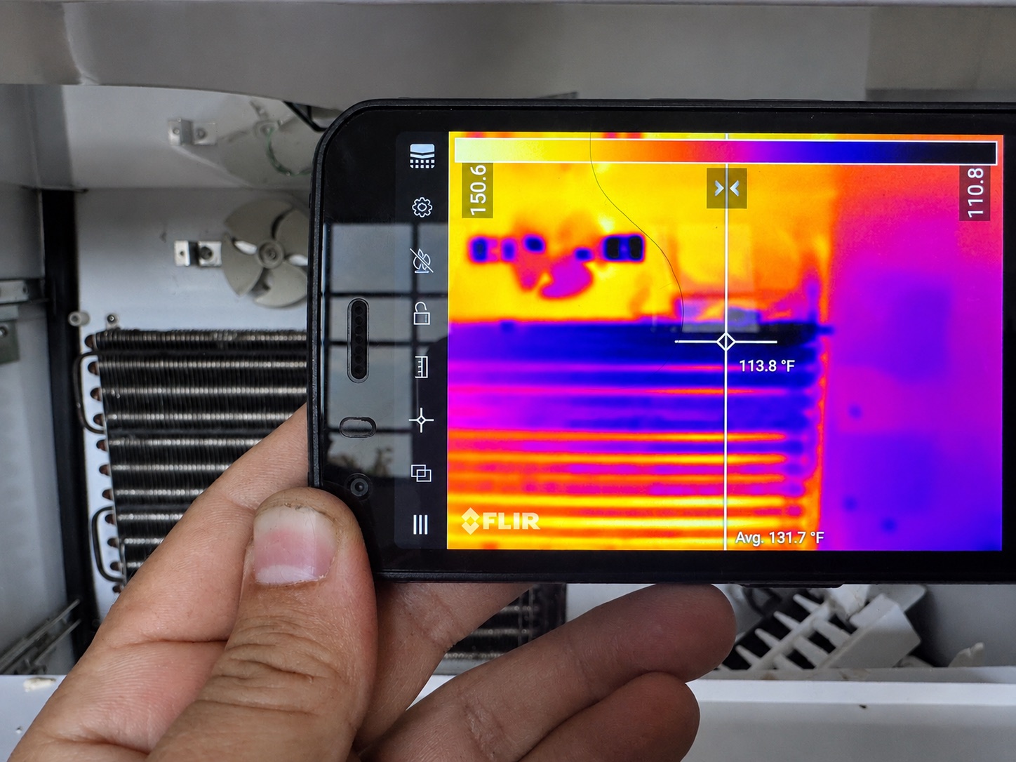 A thermal imaging camera reading temperatures across a refrigerator's condenser coil during diagnosis