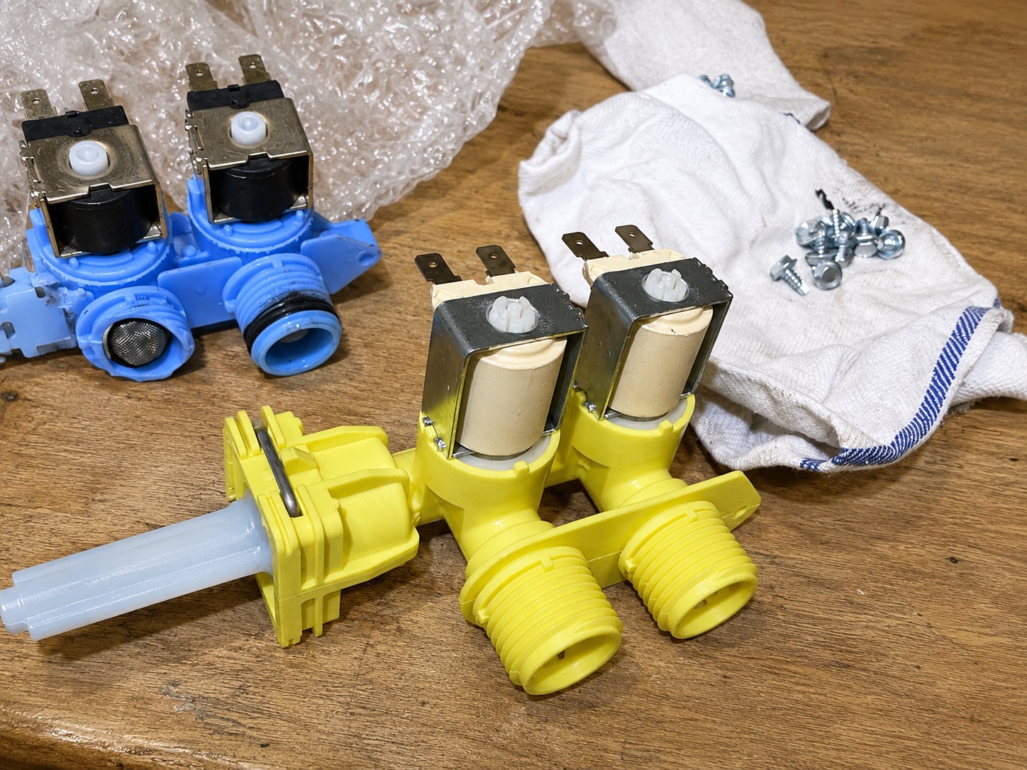 A failed water inlet valve beside its new replacement on the bench