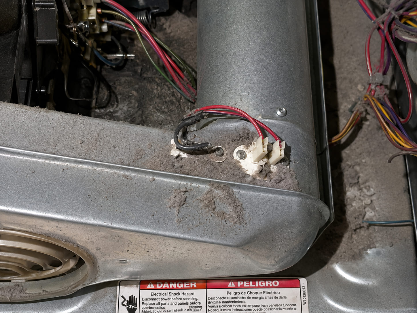 The thermal fuse and thermostat mounted on a dryer's blower housing, the metal around them furred over with packed lint