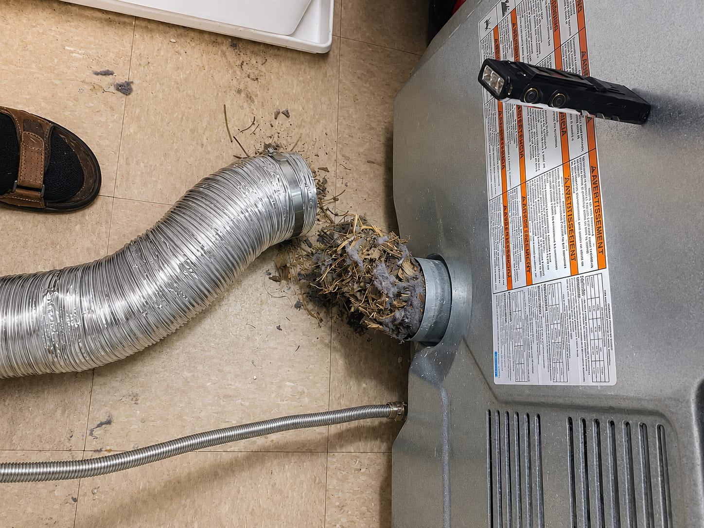 A flexible foil vent duct pulled off the back of a dryer, with a thick matted plug of lint blocking the exhaust port