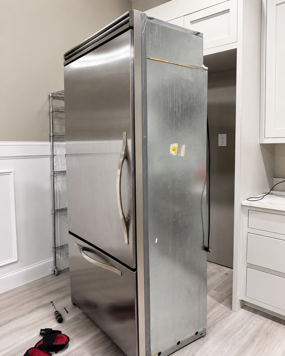 A refrigerator pulled out from its cabinet for service, tools on the floor beside it